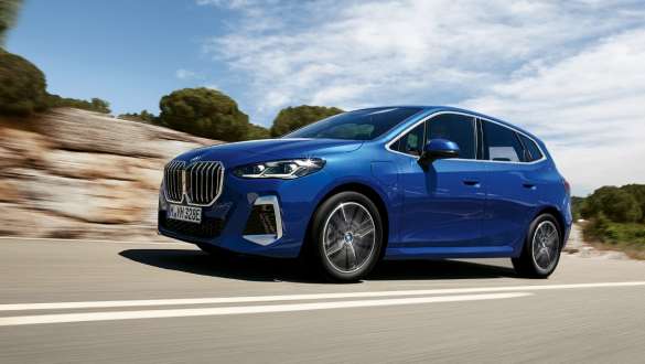 Imagine din partea laterală a BMW Seria 2 Active Tourer 230e plug-in hybrid, în Albastru Portimao M, în timp ce se deplasează pe un drum rural