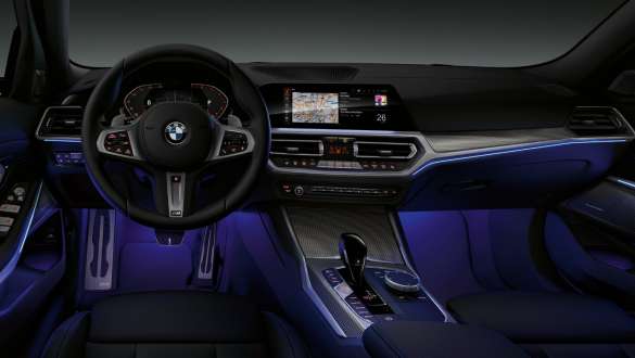 BMW Seria 3 Sedan (G20), lumină ambientală. Imagine din partea frontală a panoului de bord al şoferului BMW Seria 3 Sedan (G20) cu spaţiul pentru picioare iluminat ambiental în albastru deschis.