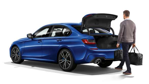 BMW Seria 3 Sedan (G20), acţionare automată a hayonului. Imagine cu trei sferturi din partea din spate a BMW Seria 3 Sedan (G20) staţionând, şoferul deschizând automat hayonul cu piciorul său.