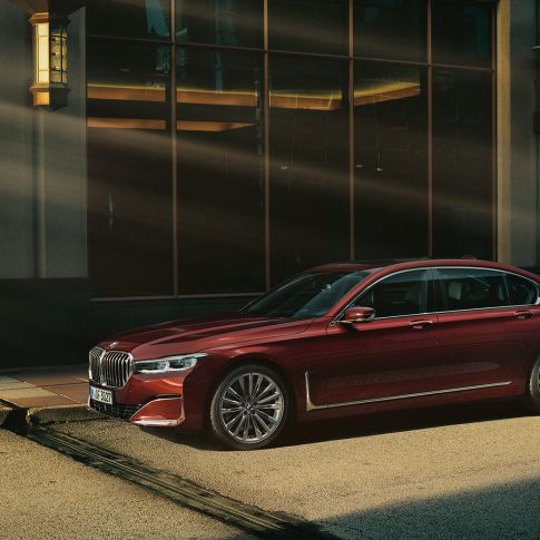 Imagine din lateral cu BMW Individual Seria 7 Sedan Imagine din lateral cu BMW Individual Seria 7 Sedan roşu în faţa unui peisaj urban