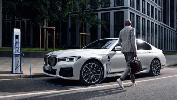 Imagine cu trei sferturi din partea laterală a unui BMW Seria 7 Sedan plug-in hybrid G11 G12 care se încarcă Imagine cu trei sferturi din partea laterală a unui BMW Seria 7 Sedan plug-in hybrid G11 G12 care se încarcă, cu un model alături