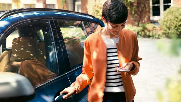 O femeie privind în smartphone-ul său şi deschizând uşa de la automobilul său BMW BMW Teleservices