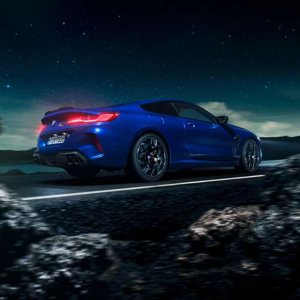 Imagine cu trei sferturi din pertea laterală a BMW M8 Competition Coupé. Imagine cu trei sferturi din partea laterală a BMW M8 Competition Coupé în Albastru Marina Bay metalizat, rulând sub cerul înstelat.