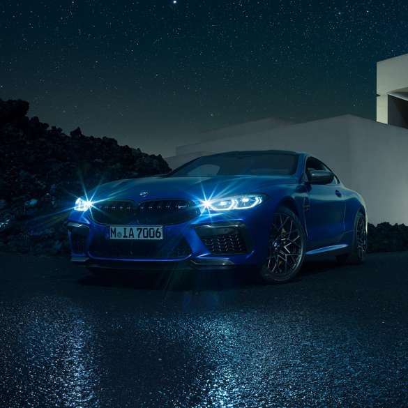 Imagine cu trei sferturi din partea frontală a BMW M8 Competition Coupé. Imagine cu trei sferturi din partea frontală a BMW M8 Competition Coupé în Albastru Marina Bay metalizat, cu faruri strălucitoare cu tehnologie LED, staţionând în faţa unei vile pe timp de noapte.