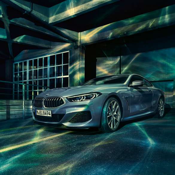 Imagine cu trei sferturi din partea frontală a BMW M850i xDrive Coupé. Imagine cu trei sferturi din partea frontală a BMW M850i xDrive Coupé în Albastru Barcelona metalizat, staţionând în faţa unei clădiri.