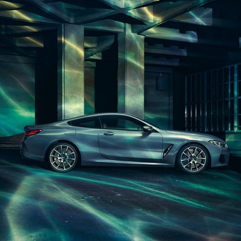 Perspectivă laterală a BMW M850i xDrive Coupé. Perspectivă laterală a BMW M850i xDrive Coupé în Albastru Barcelona metalizat, staţionând în faţa unei clădiri.