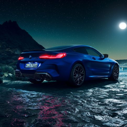 Imagine cu trei sferturi din partea spate a BMW M8 Competition Coupé. Imagine cu trei sferturi din partea spate a BMW M8 Competition Coupé în Albastru Marina Bay metalizat, cu stopuri cu tehnologie LED pornite, staţionând cu luna plină pe fundal.