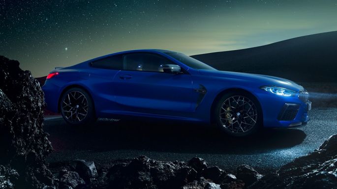 Imagine cu trei sferturi din partea laterală a BMW M8 Competition Coupé. Imagine cu trei sferturi din partea laterală a BMW M8 Competition Coupé în Albastru Marina Bay metalizat, staţionând pe timp de noapte.