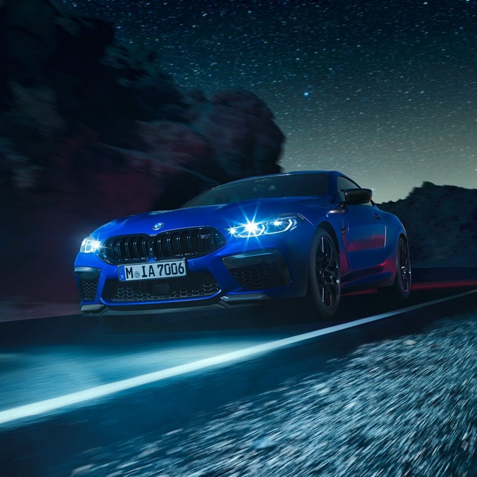 Imagine cu trei sferturi din partea frontală a BMW M8 Competition Coupé. Imagine cu trei sferturi din partea frontală a BMW M8 Competition Coupé în Albastru Marina Bay metalizat, cu faruri cu tehnologie LED pornite, rulând pe timp de noapte.