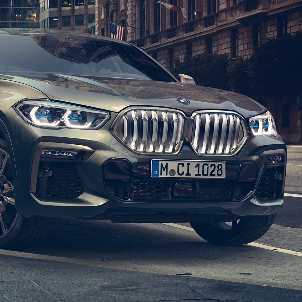 BMW X6 M50i staţionând Imagine cu trei sferturi din partea frontală a BMW X6 M50i, staţionând în faţa unui peisaj urban