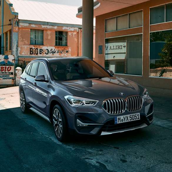 Imagine cu trei sferturi din partea frontală a BMW X1. Imagine cu trei sferturi din partea frontală a BMW X1 staţionând în faţa unui peisaj urban.