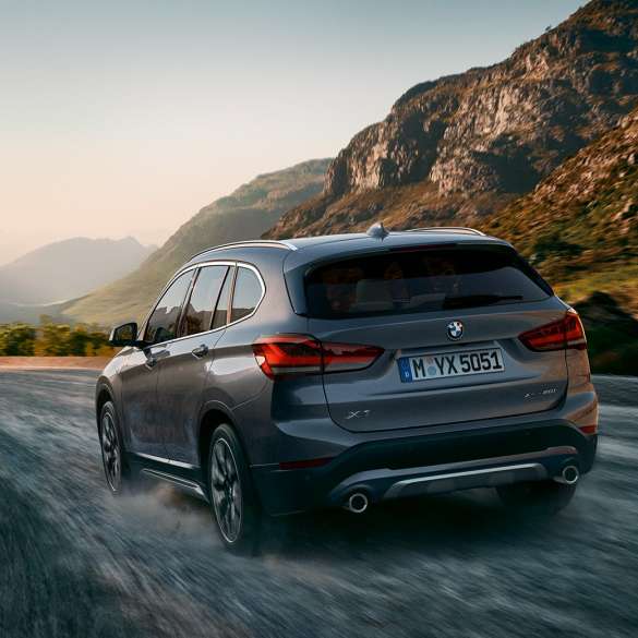 Imagine cu trei sferturi din partea spate a BMW X1. Imagine cu trei sferturi din partea spate a BMW X1 rulând într-un peisaj montan.