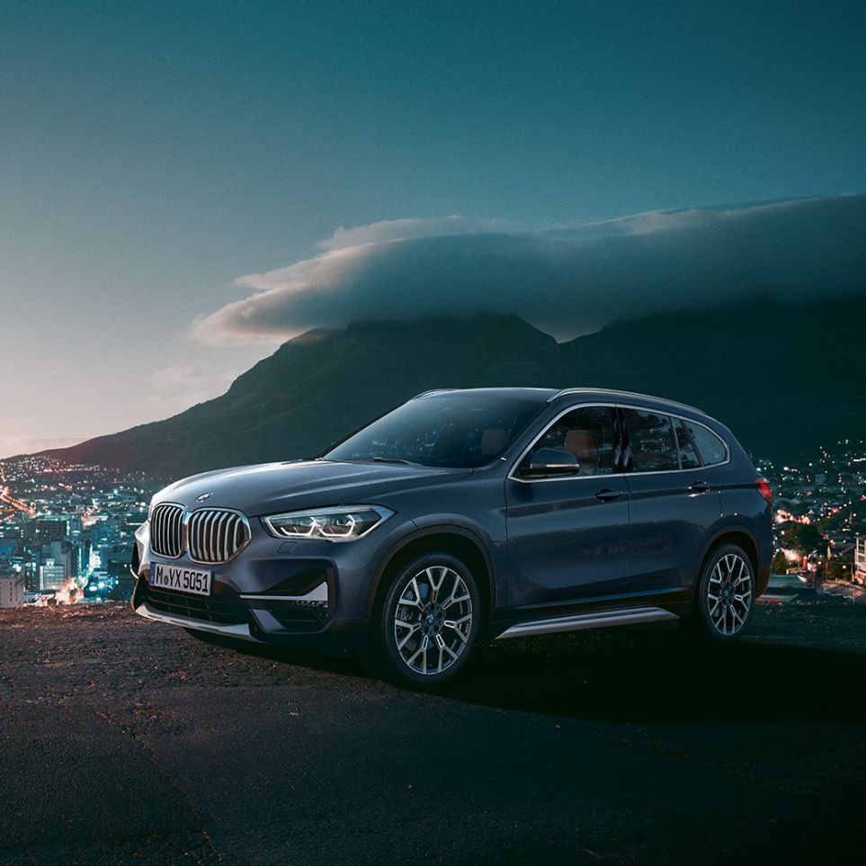 Imagine cu trei sferturi din partea laterală a BMW X1. Imagine cu trei sferturi din partea laterală a BMW X1 staţionând în faţa unui peisaj urban.