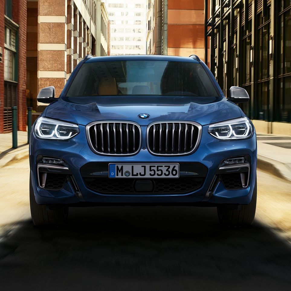 Imagine cu partea frontală a BMW X3 M40i în faţa unui peisaj urban Imagine cu partea frontală a BMW X3 M40i în faţa unui peisaj urban