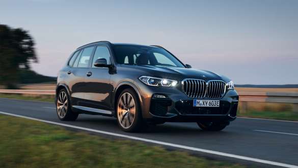 Imagine cu trei sferturi din partea frontală a modelului BMW X5 xDrive45e G05 plug-in hybrid, care se deplasează Imagine cu trei sferturi din partea frontală a modelului BMW X5 xDrive45e G05 plug-in hybrid, care se deplasează pe stradă