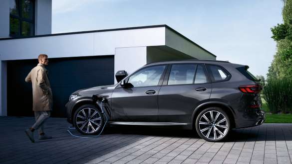 Imagine din partea laterală cu modelul BMW X5 xDrive45e G05 plug-in hybrid în faţa unui garaj Imagine din partea laterală cu modelul BMW X5 xDrive45e G05 plug-in hybrid în faţa unui garaj, cu un model
