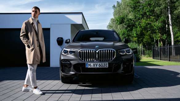Imagine din partea frontală cu modelul BMW X5 xDrive45e G05 plug-in hybrid în faţa unui garaj Imagine din partea frontală cu modelul BMW X5 xDrive45e G05 plug-in hybrid în faţa unui garaj, cu un model