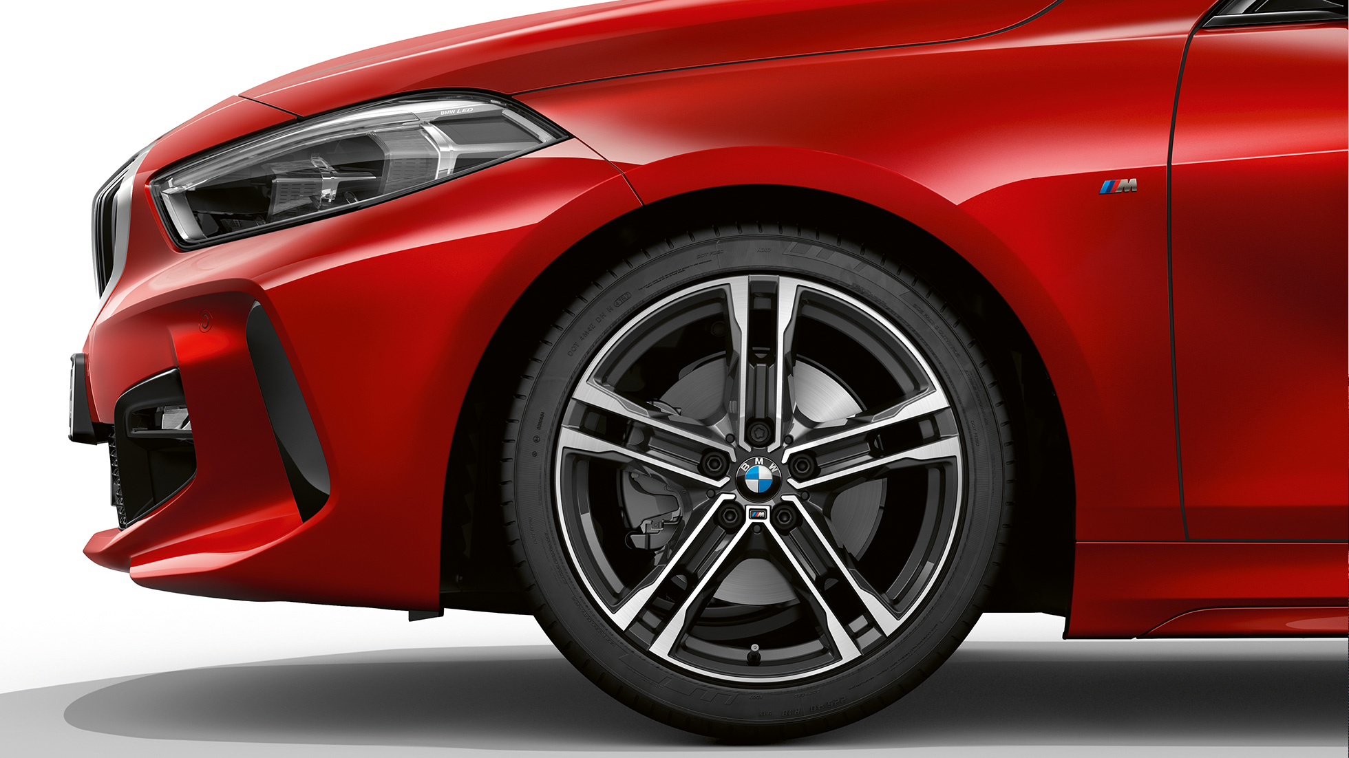 Perspectivă din lateral cu partea frontală a BMW Seria 1 Model M Sport. Perspectivă din lateral cu partea frontală a BMW Seria 1 Model M Sport în Roşu Melbourne metalizat, cu jante M din aliaj uşor de 17” Double-spoke, tip 550 M, bicolore.