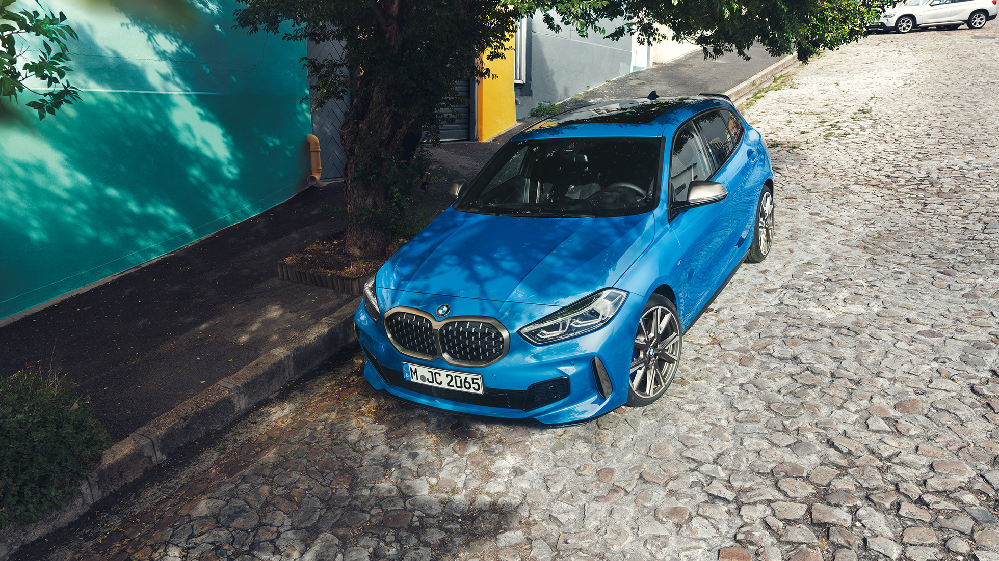 Imagine cu BMW Seria 1 pe marginea şoselei. Imagine de sus cu trei sferturi din partea frontală a BMW Seria 1 în Albastru Misano metalizat, parcând pe marginea şoselei.