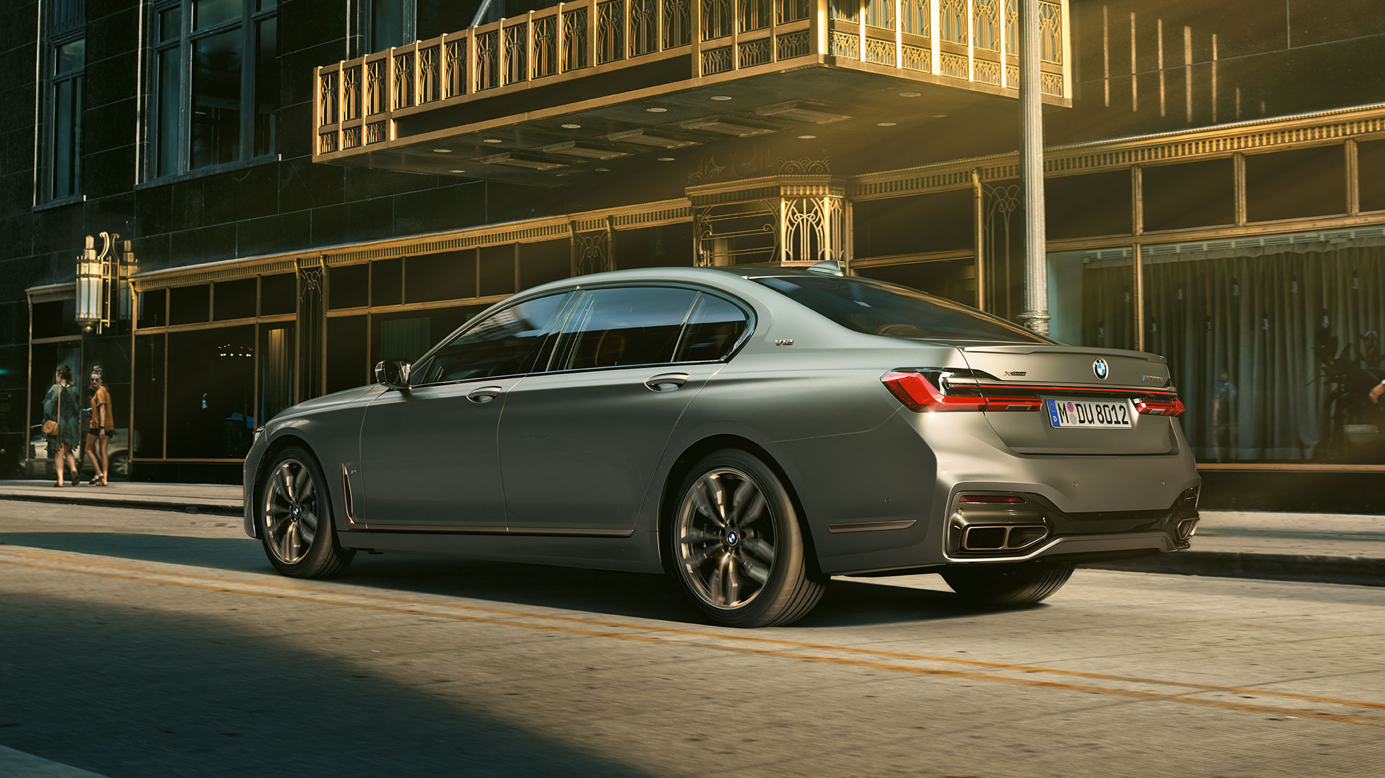 BMW M760Li xDrive cu motor V12 Perspectivă laterală din spate asupra BMW M760Li xDrive staţionând în faţa unor zgîrie-nori într-un peisaj urban