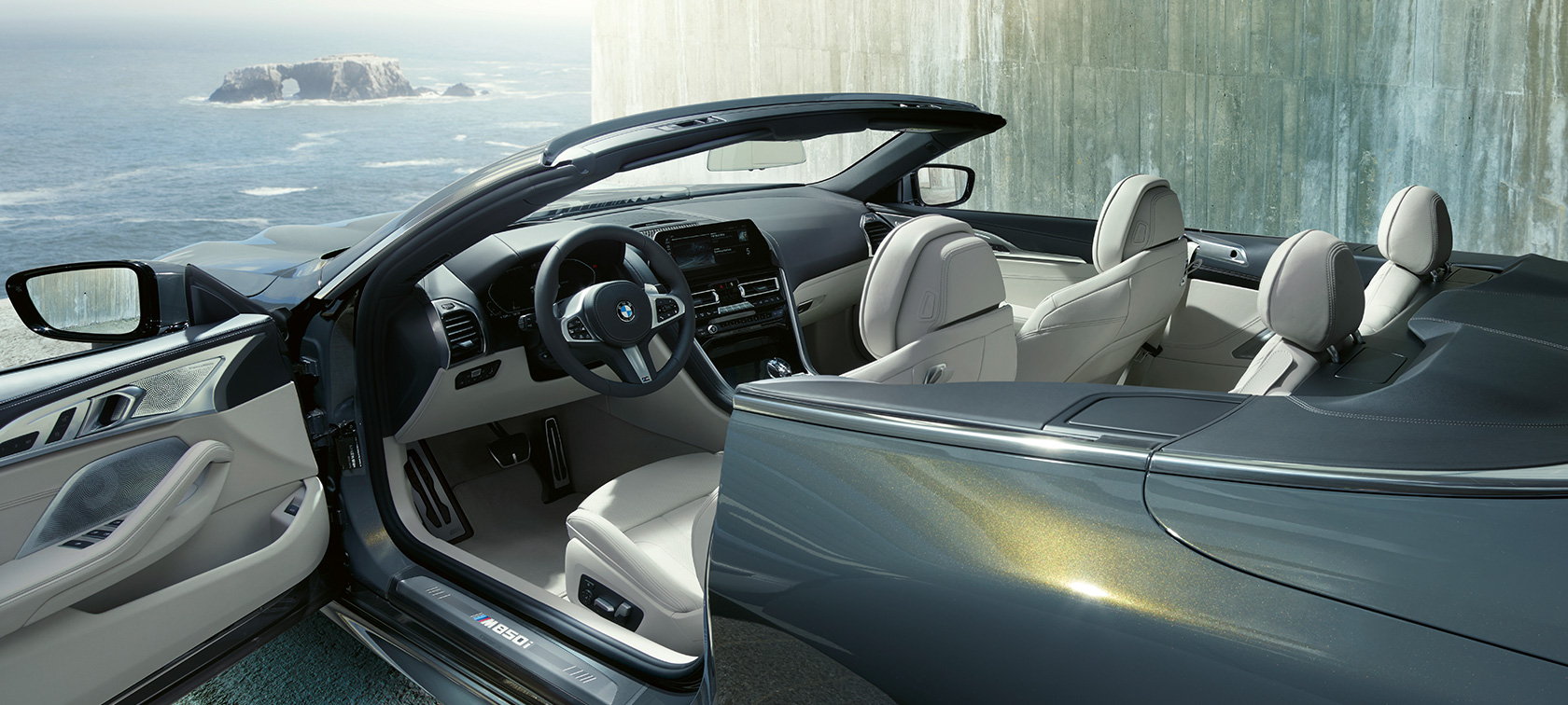 Imagine laterală a BMW M850i xDrive în Gri Dravit metalizat, cu soft-top-ul şi portiera deschise. Imagine laterală a BMW M850i xDrive în Gri Dravit metalizat, cu soft-top-ul şi portiera deschise.