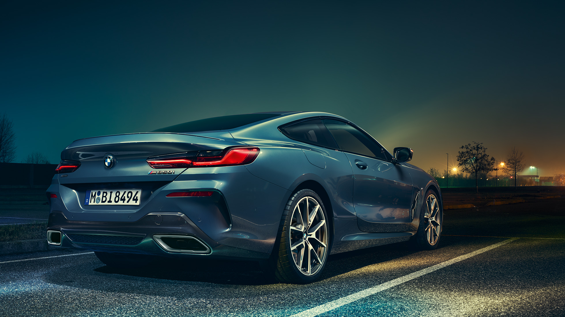 Imagine cu trei sferturi din partea spate a BMW Seria 8 Coupé. Imagine cu trei sferturi din partea spate a BMW Seria 8 Coupé, staţionând în faţa unui peisaj nocturn.