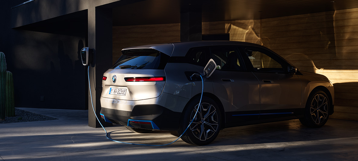 Imagine cu trei sferturi din partea din spate a BMW iX, încărcare la BMW Wallbox Imagine cu trei sferturi din partea din spate a BMW iX i20, Argintiu Cashmere, încărcare la BMW Wallbox