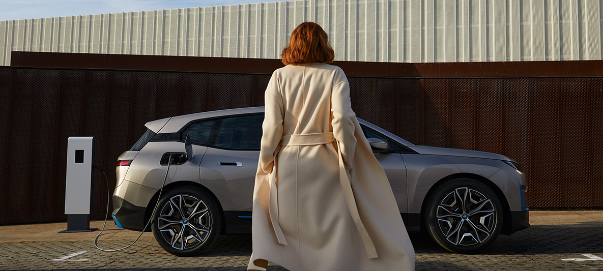 Imagine din partea laterală a BMW iX, staţionând Imagine din partea laterală a BMW iX i20, Argintiu Cashmere, staţionând, cu un model în faţă