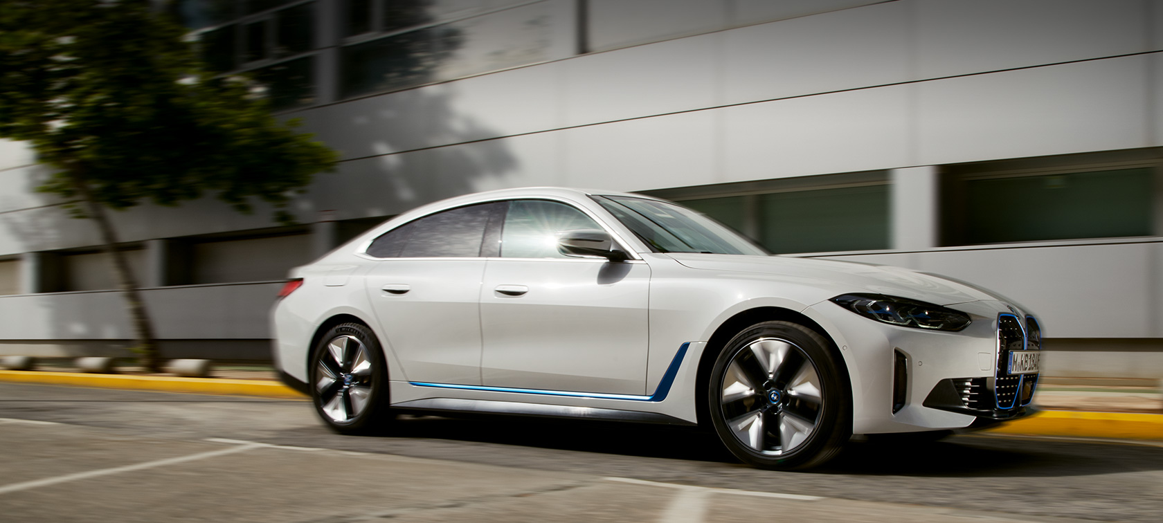 Imagine cu trei sferturi din partea laterală a unui BMW i4 eDrive40 G26 2021 rulând în faţa unei clădiri Imagine cu trei sferturi din partea laterală a unui BMW i4 eDrive40 G26 2021 rulând în faţa unei clădiri