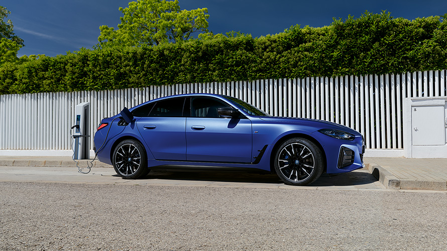Imagine din partea laterală a unui BMW i4 M50 G26 2021 Imagine din partea laterală a unui BMW i4 M50 G26 2021 BMW Individual Albastru Frozen Portimao care este la un stâlp de încărcare