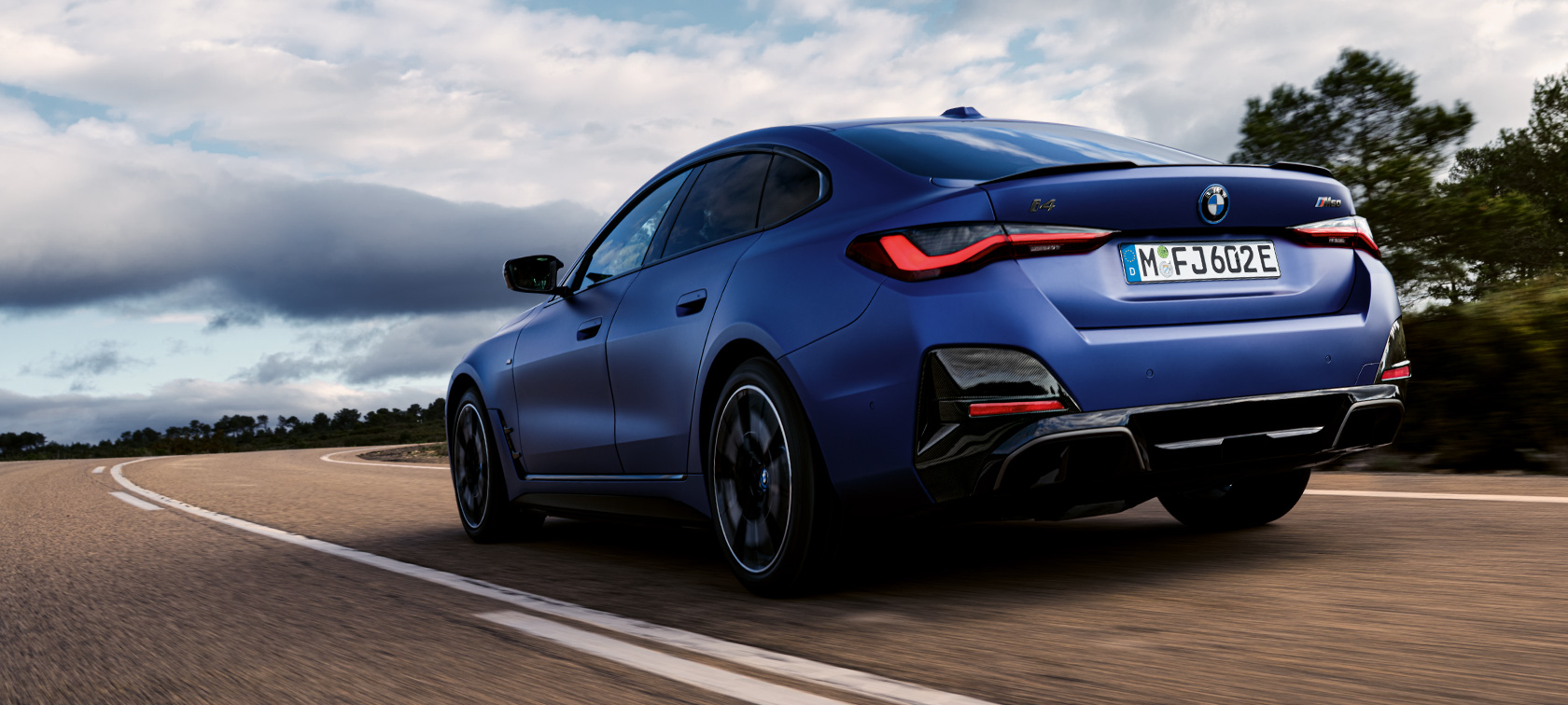 Imagine cu trei sferturi din partea din spate a unui BMW i4 M50 G26 2021 Imagine cu trei sferturi din partea din spate a unui BMW i4 M50 G26 2021 BMW Individual Albastru Frozen Portimao în timp ce se deplasează
