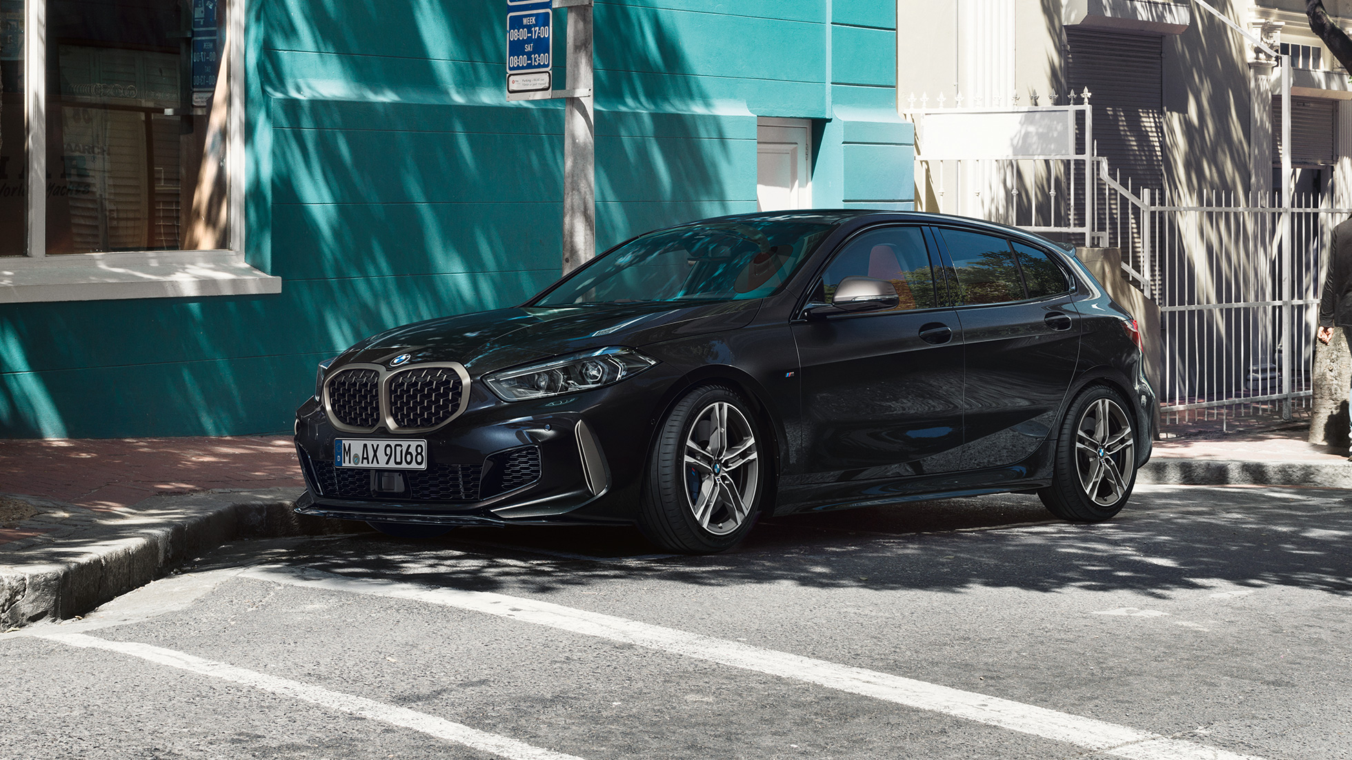 Imagine cu trei sferturi din partea laterală a BMW M135i xDrive. Imagine cu trei sferturi din partea laterală a noului BMW M135i xDrive în Negru Sapphire metalizat, parcând.