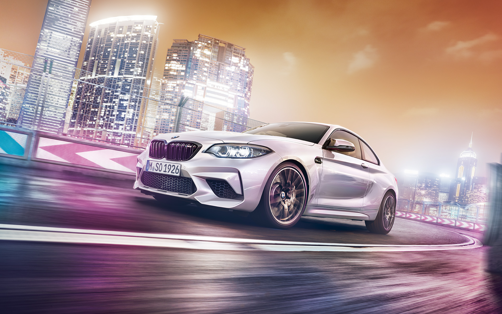 Automobil BMW M2 Competition la orizont Automobil BMW M2 Competition alb condus pe circuitul de curse în faţa unui orizont nocturn.