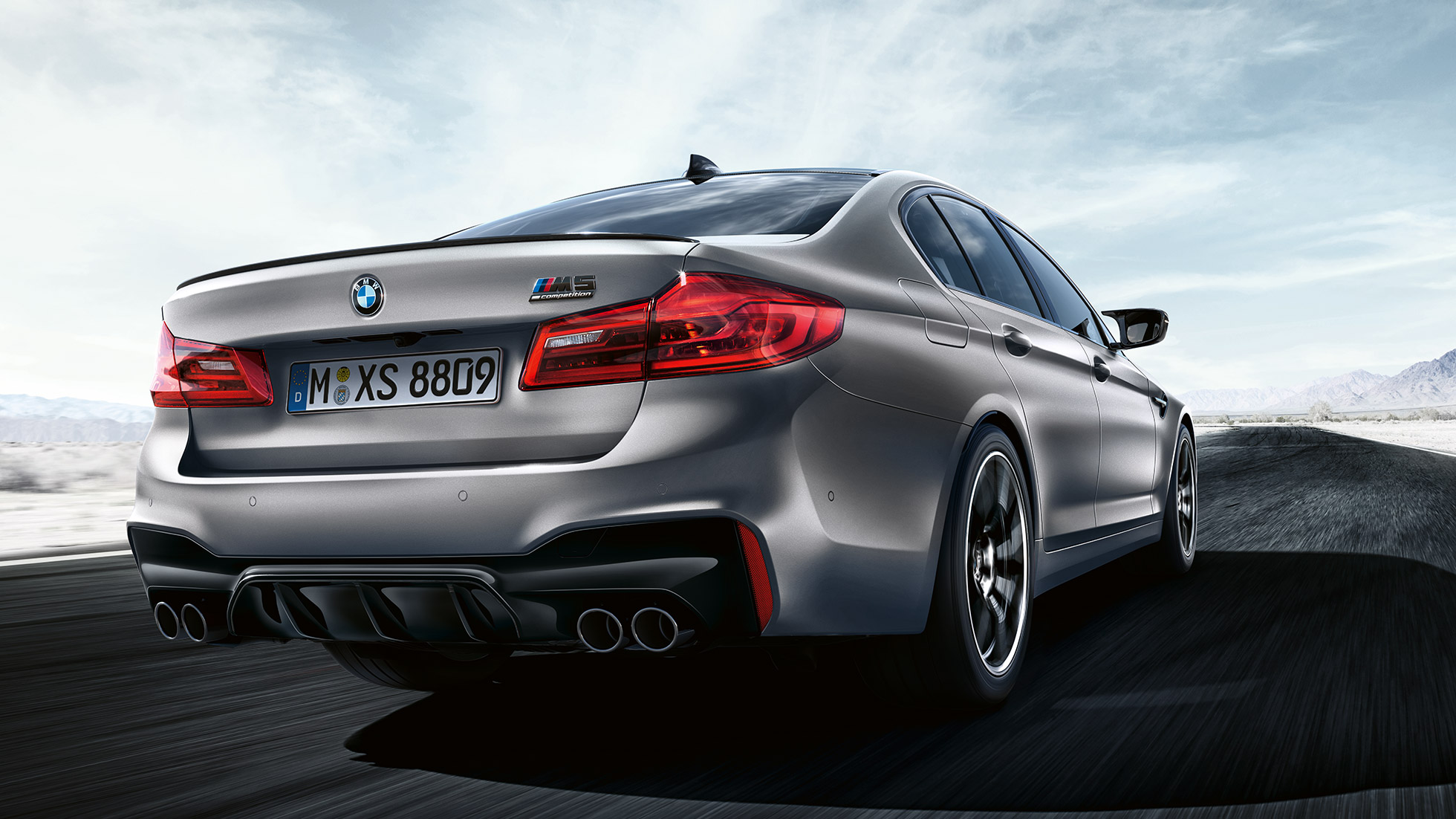 Stopuri cu tehnologie LED. Imagine cu trei sferturi din partea spate a BMW M5 Competition cu design specific.