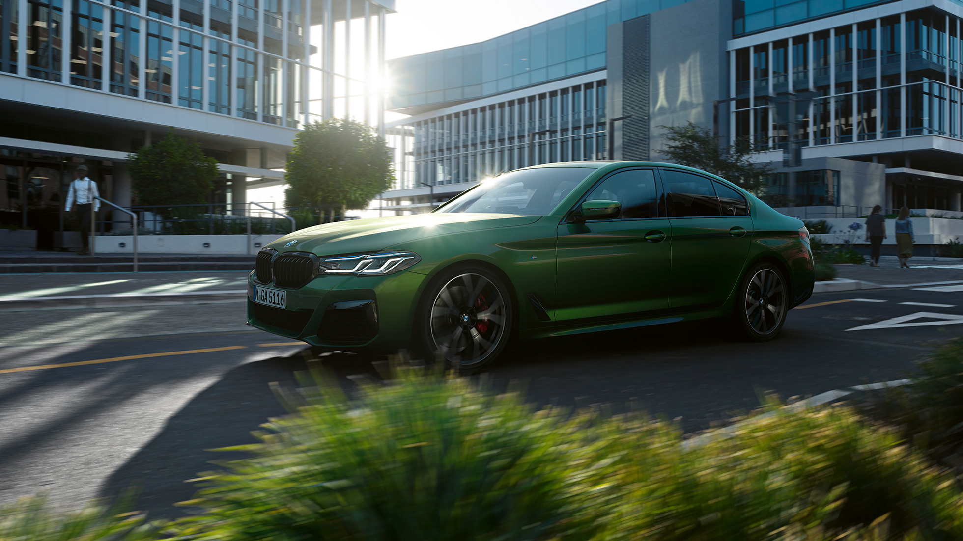Imagine cu partea laterală a BMW M550i xDrive Sedan, G30, LCI, Facelift, 2020, rulând Imagine cu partea laterală a BMW M550i xDrive Sedan, G30, LCI, Facelift, 2020, în Verde Ermes metalizat de la BMW Individual, rulând prin centrul oraşului