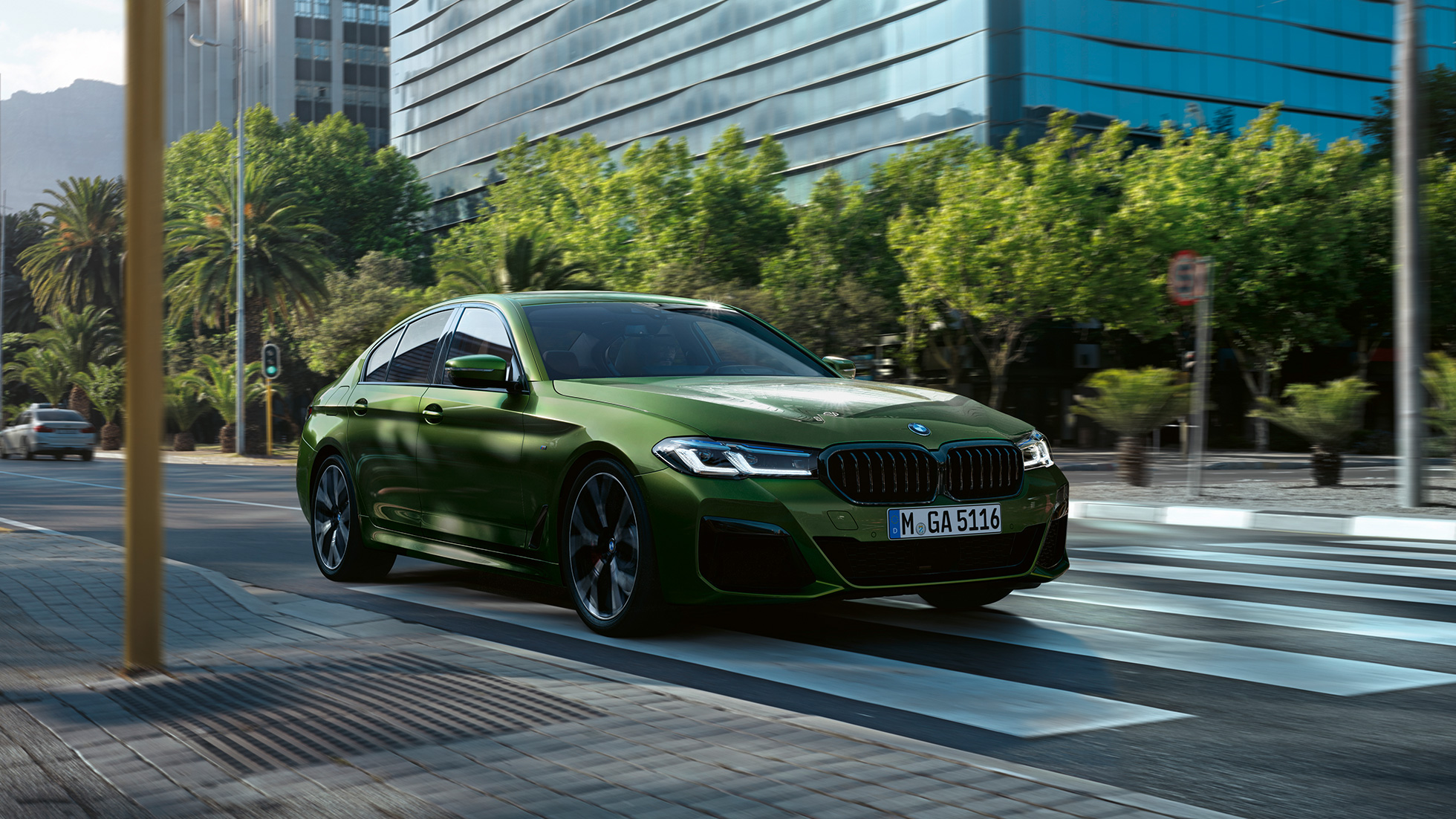 Imagine cu trei sferturi din partea frontală a BMW M550i xDrive Sedan, G30, LCI, Facelift, 2020, rulând Imagine cu trei sferturi din partea frontală a BMW M550i xDrive Sedan, G30, LCI, Facelift, 2020, în Verde Ermes metalizat de la BMW Individual, rulând prin centrul oraşului