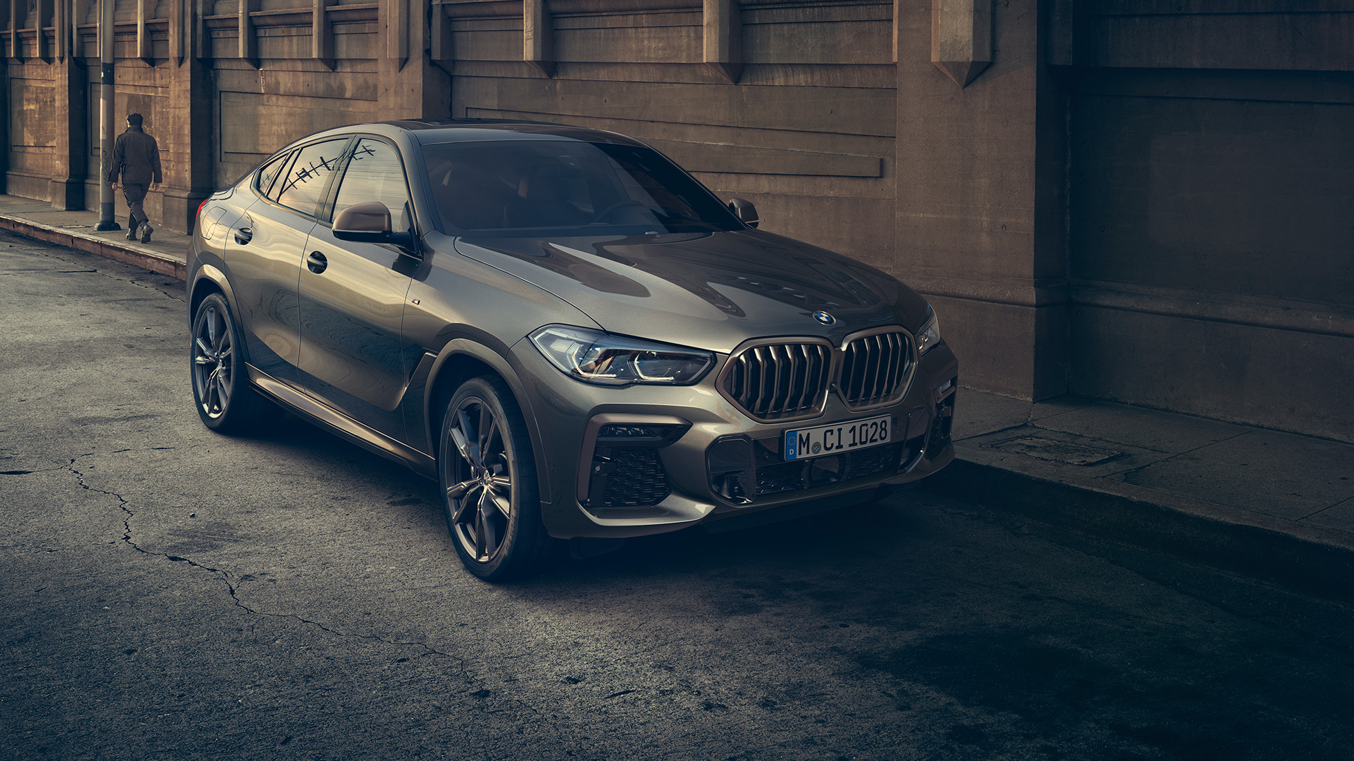 BMW X6 M50i, staţionând. Perspectivă frontală cu trei sferturi din BMW X6 M50i, staţionând în faţa unui fundal urban.