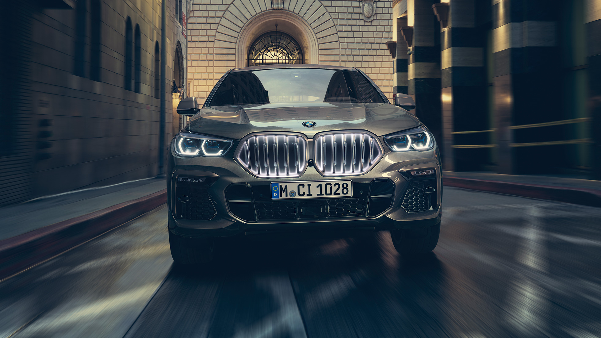 BMW X6 M50i cu grilă BMW „Iconic Glow”. Perspectivă frontală a BMW X6 M50i, staţionând în faţa unui fundal urban.