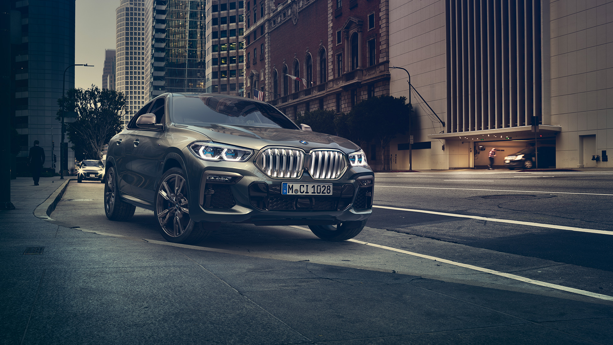 BMW X6 M50i, staţionând. Perspectivă frontală cu trei sferturi din BMW X6 M50i, staţionând în faţa unui fundal urban.