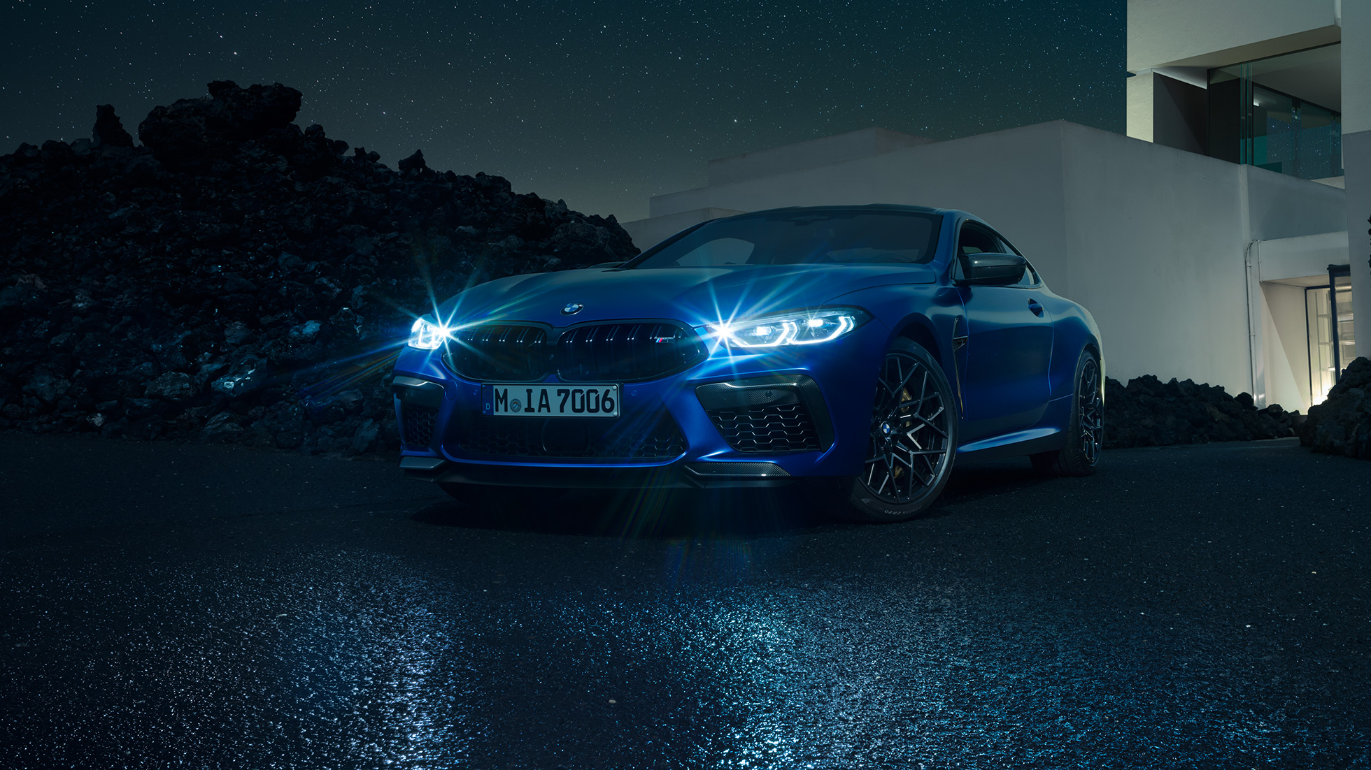 Imagine cu trei sferturi din partea frontală a BMW M8 Competition Coupé. Imagine cu trei sferturi din partea frontală a BMW M8 Competition Coupé în Albastru Marina Bay metalizat, cu faruri strălucitoare cu tehnologie LED, staţionând în faţa unei vile pe timp de noapte.