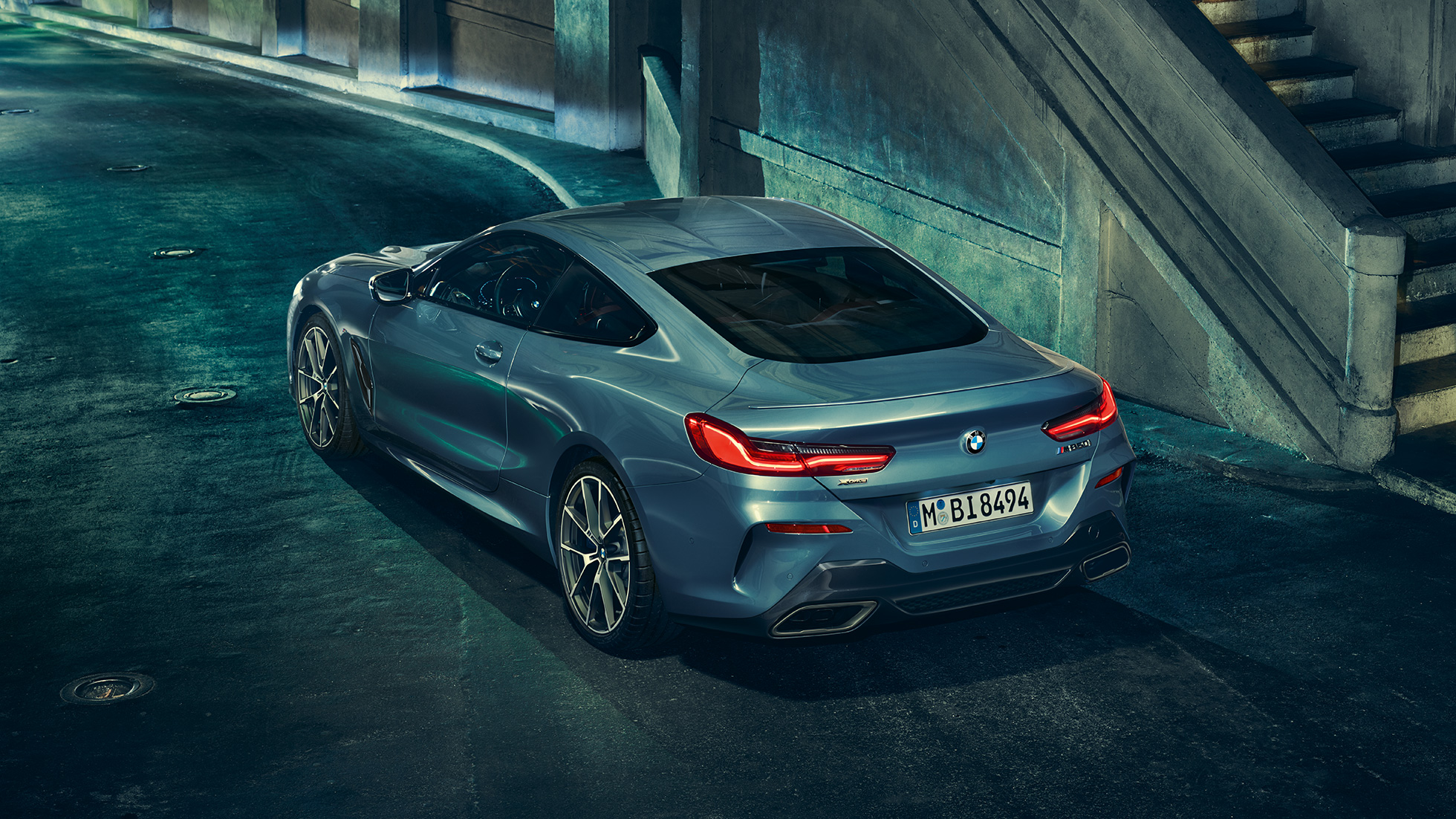 Imagine cu trei sferturi din partea spate stânga a BMW M850i xDrive Coupé. Imagine cu trei sferturi din partea spate stânga a BMW M850i xDrive Coupé în Albastru Barcelona metalizat, staţionând pe timp de noapte.