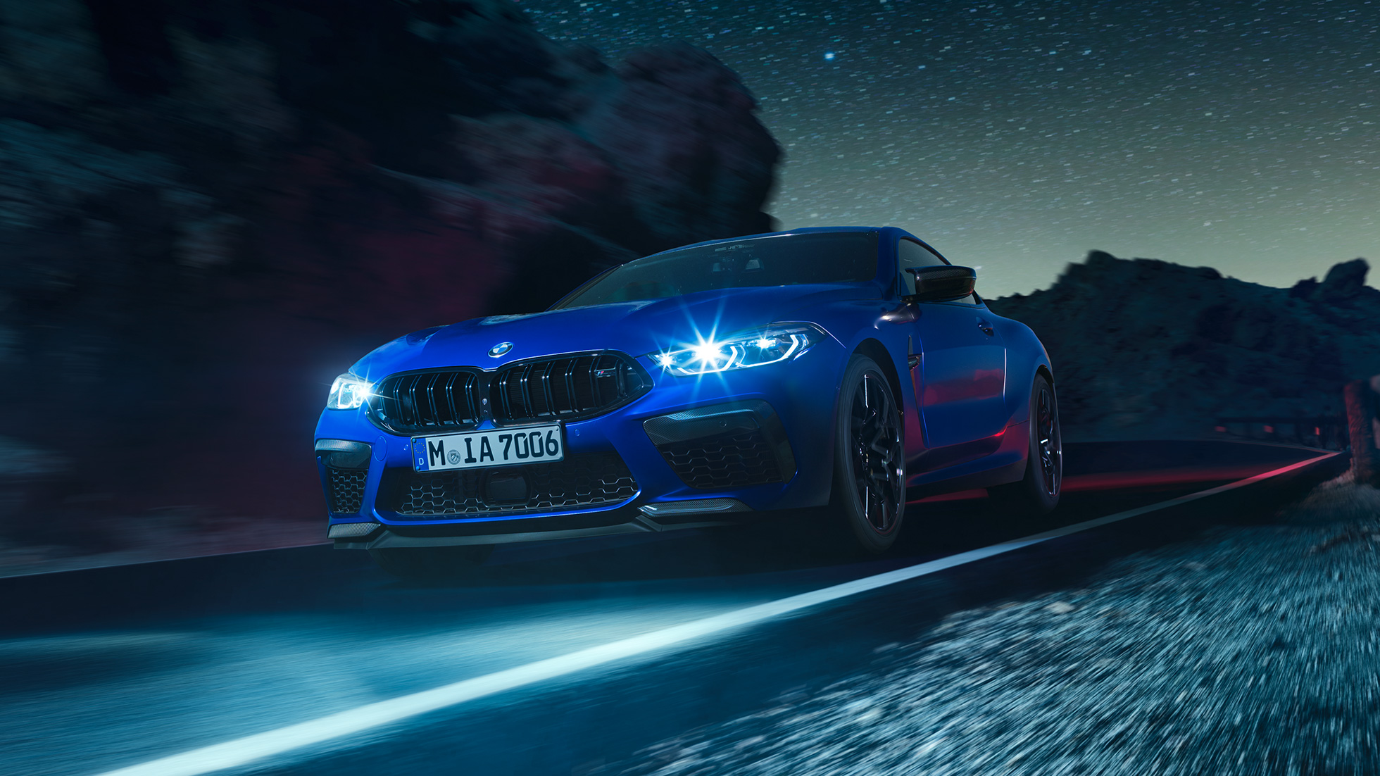Imagine cu trei sferturi din partea frontală a BMW M8 Competition Coupé. Imagine cu trei sferturi din partea frontală a BMW M8 Competition Coupé în Albastru Marina Bay metalizat, cu faruri cu tehnologie LED pornite, rulând pe timp de noapte.