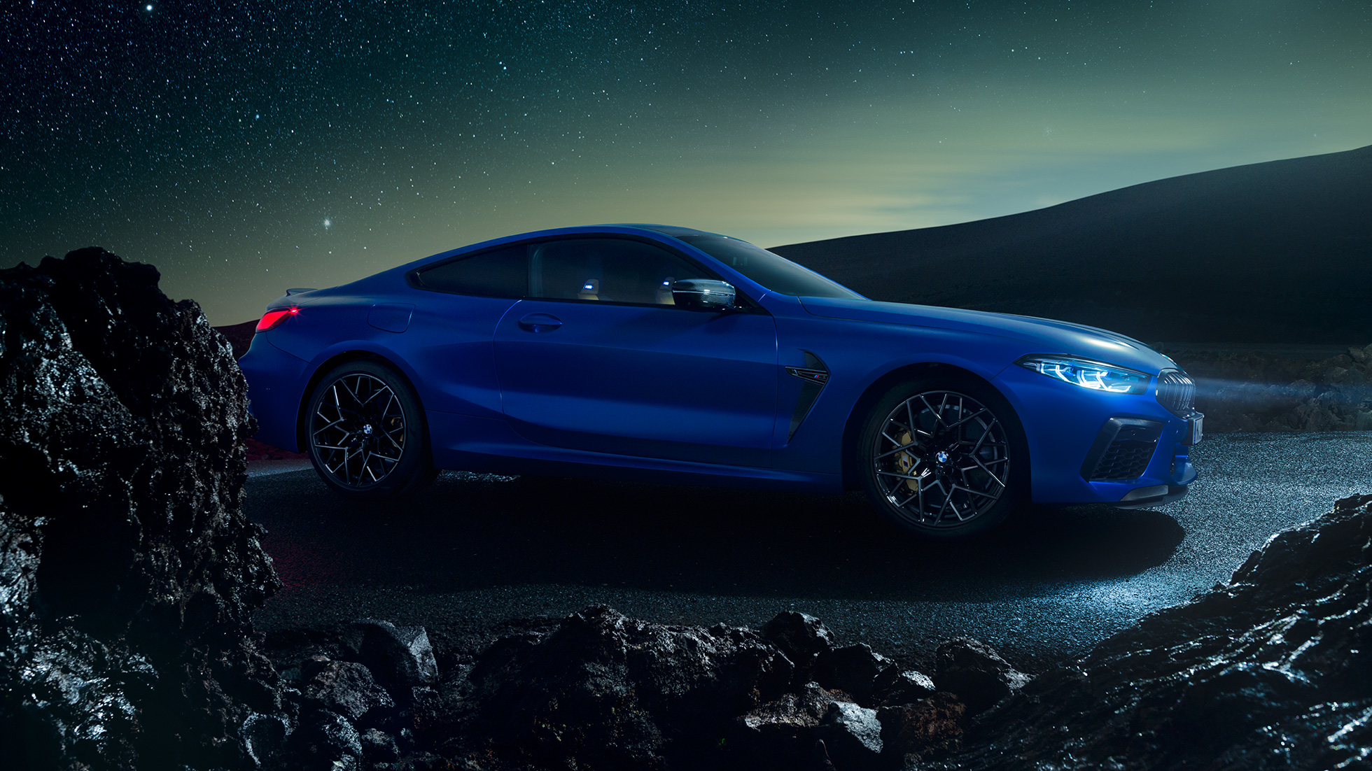 Imagine cu trei sferturi din partea laterală a BMW M8 Competition Coupé. Imagine cu trei sferturi din partea laterală a BMW M8 Competition Coupé în Albastru Marina Bay metalizat, staţionând pe timp de noapte.