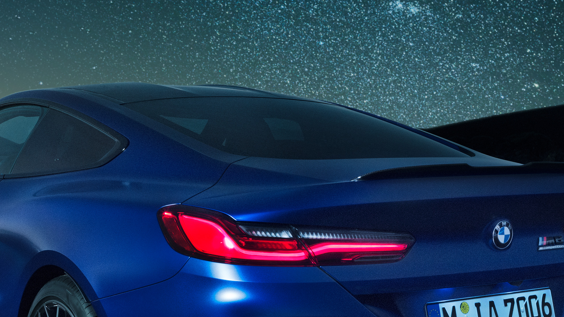 Spoiler M pentru partea spate Imagine în prim-plan cu secţiunea umărului BMW M8 Competition Coupé în Albastru Marina Bay metalizat, cu spoiler M pentru partea spate din carbon, pe timp de noapte.