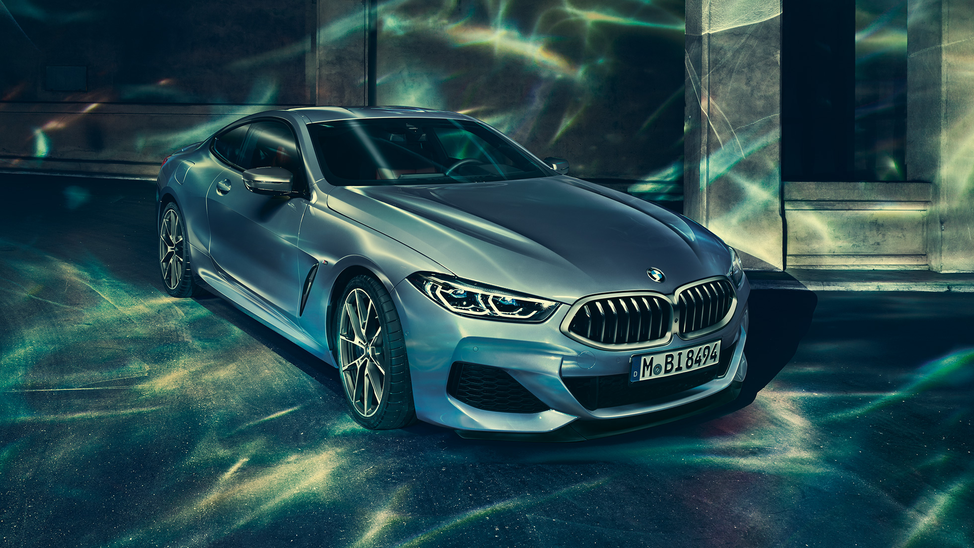 Imagine cu trei sferturi din partea frontală stânga a BMW M850i xDrive Coupé. Imagine cu trei sferturi din partea frontală stânga a BMW M850i xDrive Coupé în Albastru Barcelona metalizat, staţionând în faţa unei clădiri.