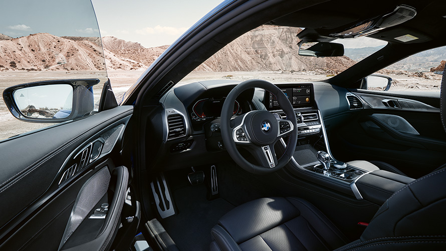 BMW M850i xDrive Coupé, habitaclu orientat spre conducător auto cu volan M îmbrăcat în piele, portieră faţă deschisă