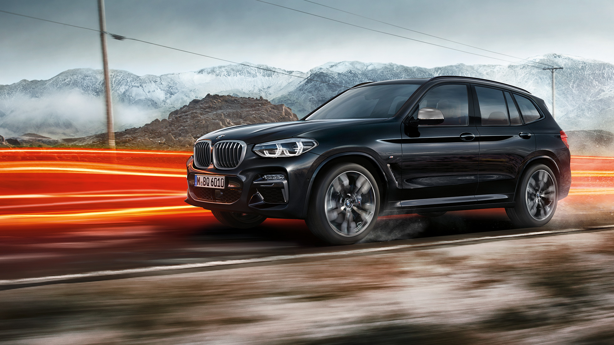 Perspectivă laterală a BMW X3 M40i şi BMW X3 M40d. Perspectivă laterală a exteriorului BMW X3 M40i şi BMW X3 M40d în Negru Sapphire metalizat rulând într-un peisaj montan cu raze de lumină.
