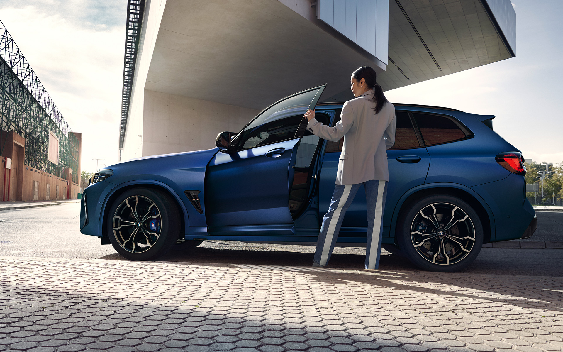 Imagine din partea laterală a unui BMW X3 M Competition F97 LCI Facelift 2021 în Albastru Frozen Marina Bay, cu portiera deschisă şi model feminin