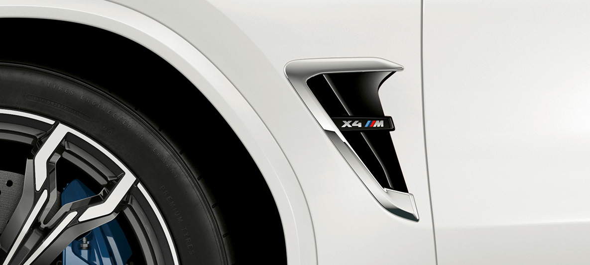 Imagine cu BMW X4 M, cu prize de aer M laterale. Imagine cu partea exterioară a BMW X4 M în Alb Alpine, cu prize de aer M laterale cu detalii cromate şi inscripţionarea denumirii modelului.
