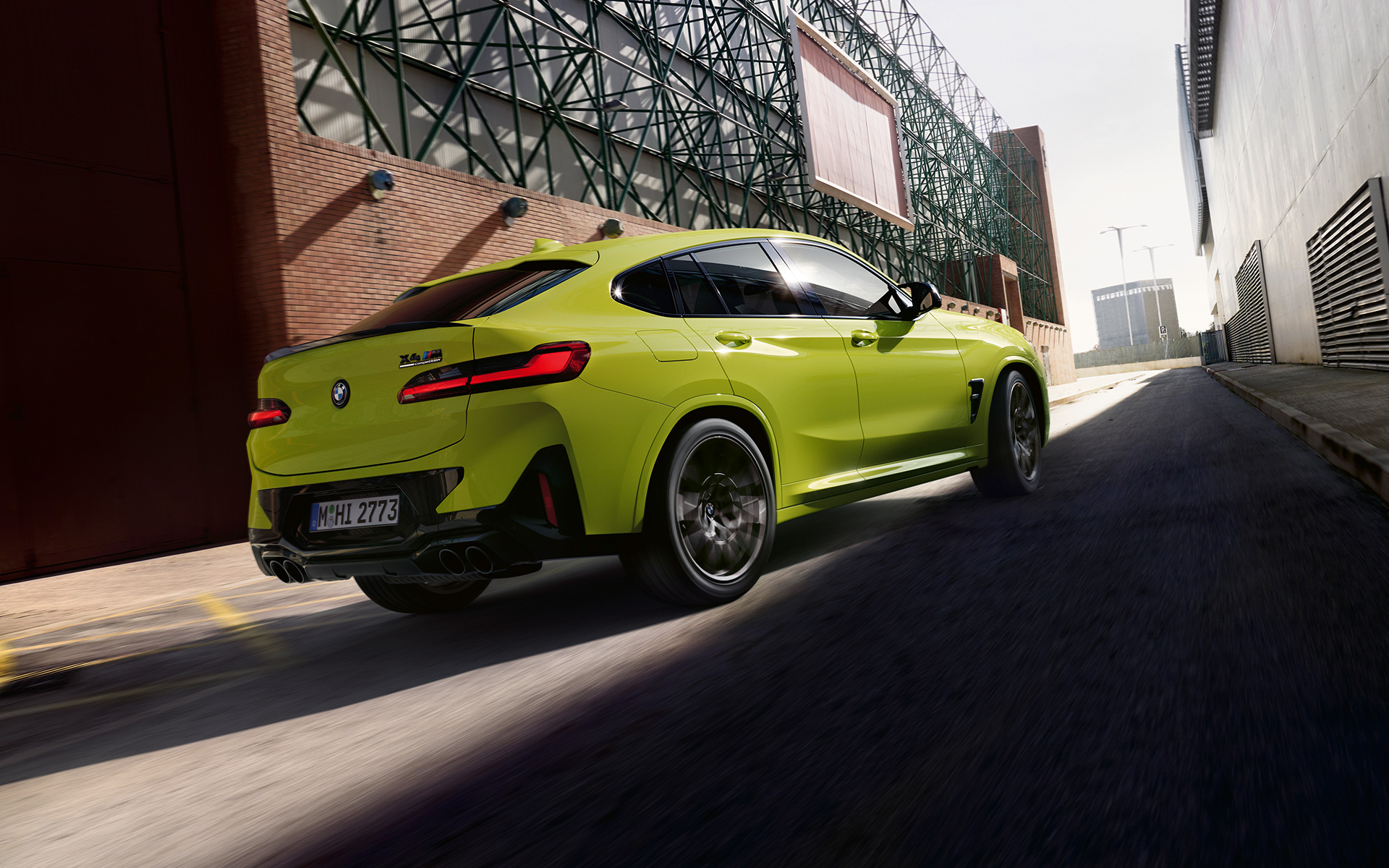 Imagine cu trei sferturi din partea frontală a unui BMW X4 M Competition F98 LCI 2021 Galben Sao Paulo care se deplasează într-o zonă industrială